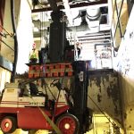 Lowering 14,500 lb. low-headroom lift truck into basement area using a Versa-Lift™ Model 25/35 with boom hoist attachment. Note the Versa-Lift™ is on a cribbed and plated platform level with the floor, enabling the lift to access the opening