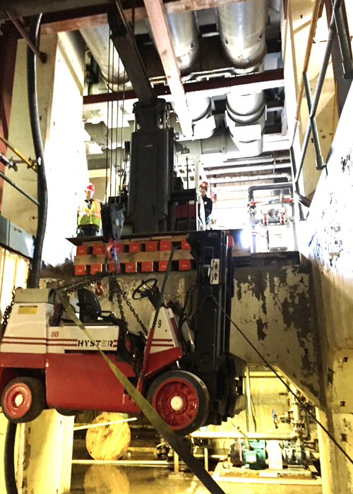 Lowering 14,500 lb. low-headroom lift truck into basement area using a Versa-Lift™ Model 25/35 with boom hoist attachment. Note the Versa-Lift™ is on a cribbed and plated platform level with the floor, enabling the lift to access the opening.